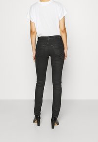 Jeans negros ajustados con un corte elegante, que cuentan con bolsillos traseros y una cinturilla de altura media. Combinados con una camiseta blanca holgada y tacones altos.