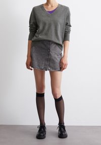 Harmaa V-pääntie neule, jossa on ribbireunat, yhdistettynä haalistuneesta mustasta denimihameeseen. Mustat polven yli ulottuvat sukat ja jykevät mustat kengät täydentävät asua.