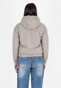 Giacca a vento grigia chiara, con cappuccio, polsini elastici e design corto. Indossata con jeans larghi di colore azzurro.