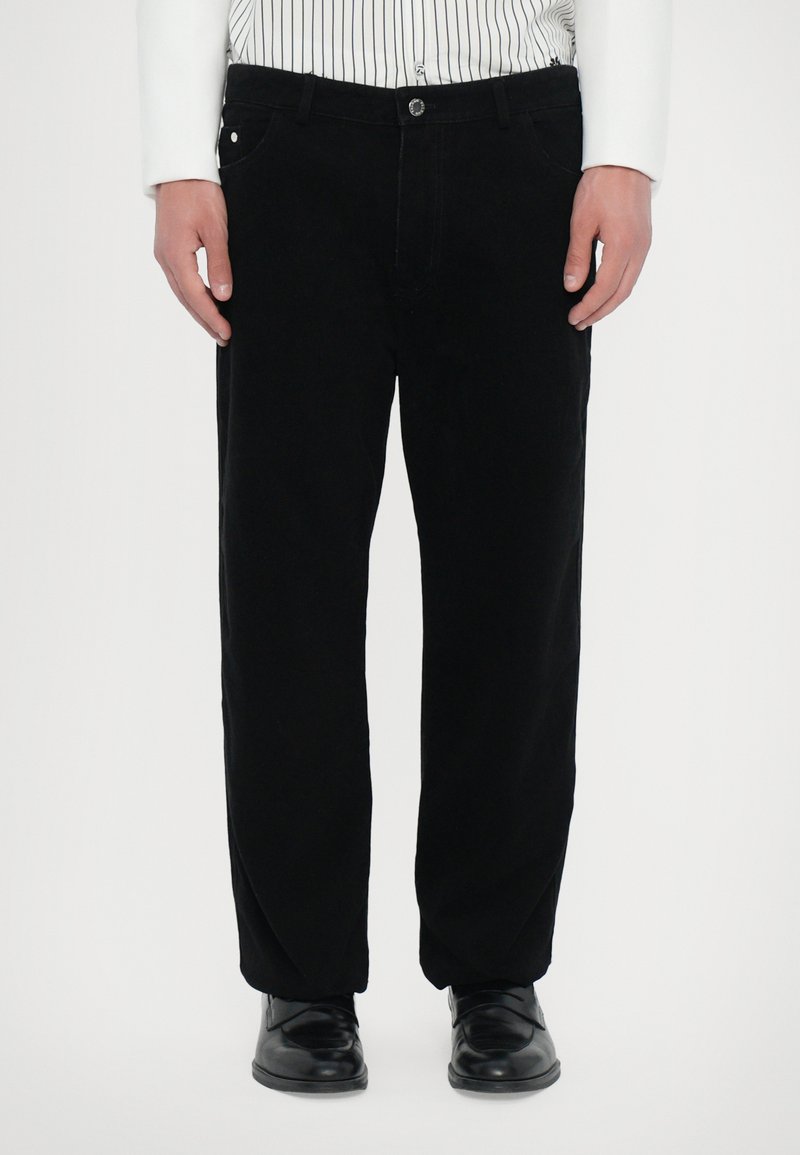 Pantalons en velours côtelé noirs avec une coupe droite, comprenant des poches avant, une fermeture à bouton et une texture lisse. Assortis avec des chaussures noires.