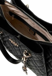 Sac à main matelassé noir avec ferrures dorées, fermeture éclair et doublure intérieure arborant le nom de la marque. Comprend un charm décoratif.