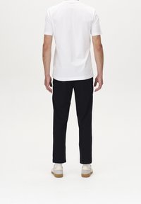 White short-sleeve T-shirt and black pants worn with grey and white shoes, standing against a plain light background.