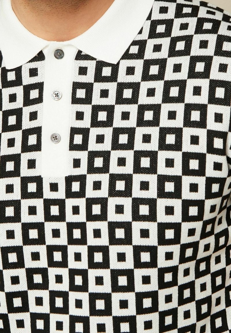 Gros plan d'une chemise à carreaux noire et blanche avec un col blanc et trois boutons gris.
