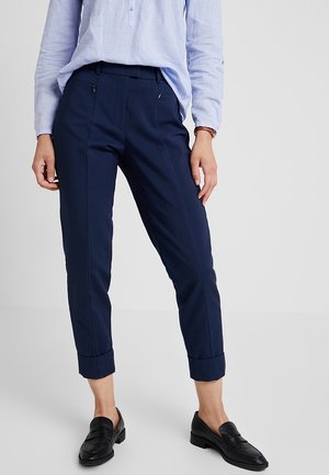 Marineblau maßgeschneiderte Hose mit Fronttaschen, gekrempelten Säumen und glatter Textur, kombiniert mit einem himmelblauen Hemd und schwarzen Mokassins.