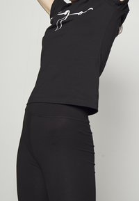 Schwarzes T-Shirt mit kurzen Ärmeln und lockerer Passform, mit einem weißen Grafikdesign auf der Vorderseite, kombiniert mit schwarzen enganliegenden Leggings.