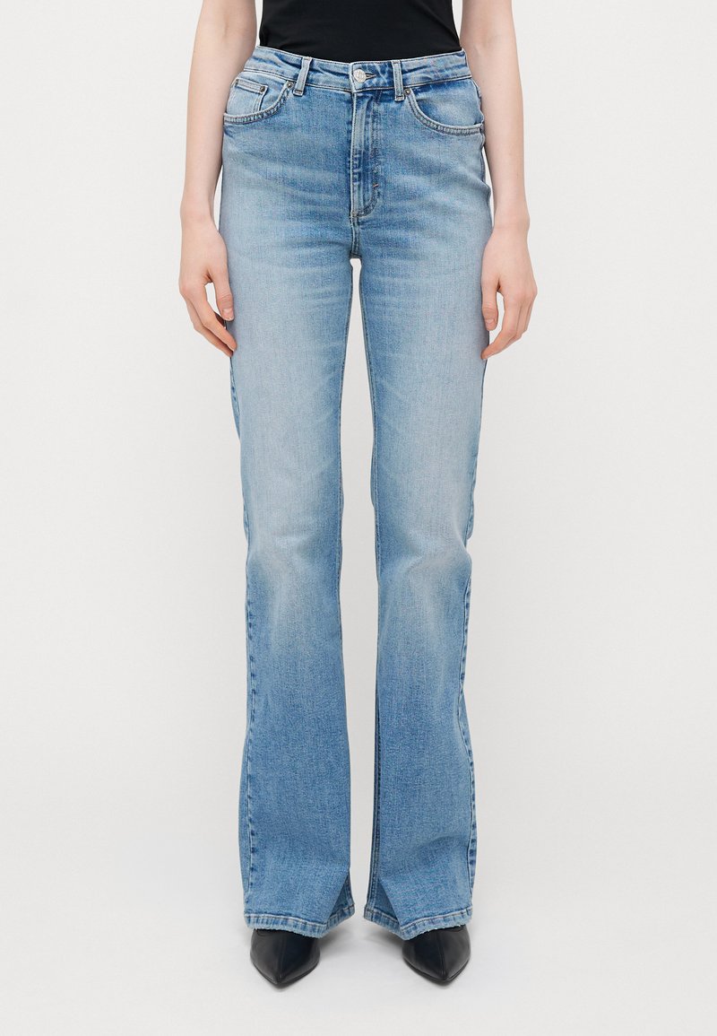 Calças de ganga azuis claras, com corte largo, apresentando cinco bolsos, cintura média e um ligeiro desgaste. A bainha tem um detalhe em fenda.