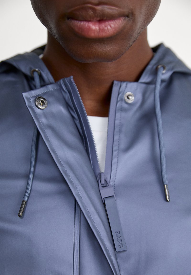 Lichtblauwe regenjas met een gladde, waterdichte textuur, verstelbare trekkoorden en zilveren hardware-details bij de rits.