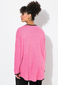 Rosa tröja med lös passform, lång ärm och rund halsringning. Har svart trim längs halsringningen och ärmarna, med en mjuk textur.