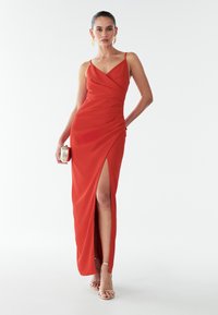 Punane, põrandani ulatuv kleit V-dekolteega ja korjetega detailides. Omab reie kõrgust lõhet ja õhukesi õlgenöörid. Sile kangas.