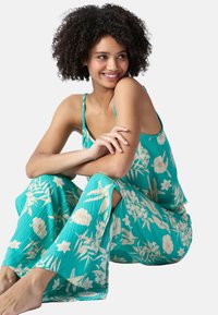 En turkos blommig jumpsuit med krämfärgade mönster, med vida ben och sidoflikar, tillverkad av lätt, texturerad tyg.