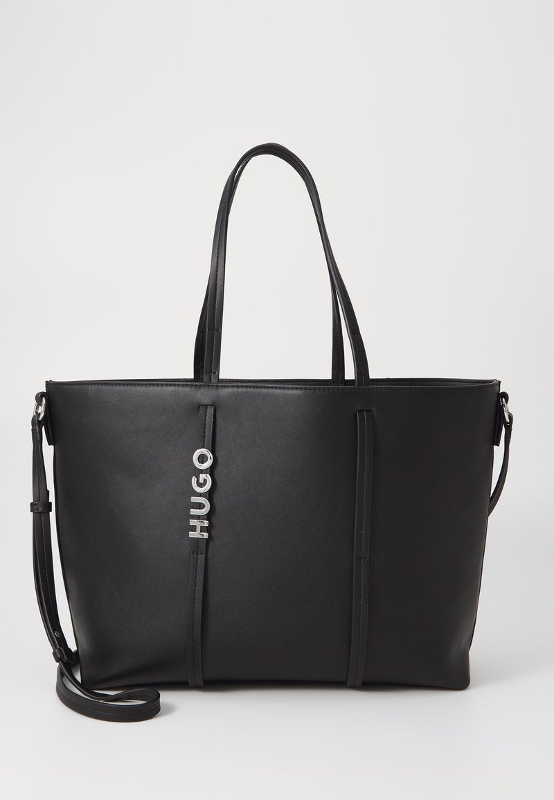 Sac fourre-tout en synthétique noir avec deux longues poignées, arborant un logo "HUGO" argenté et un design minimaliste. Texture lisse, forme rectangulaire.