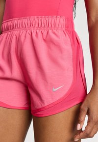 Rožinės sportinės šortai su elastingu juosmeniu, turintys tinklinį šoniniame pane, ir mažą sidabrinę Nike logotipą ant krašto.