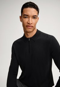 Schwarzes Langarm-Polohemd mit einem Reißverschlusskragen. Weiches, gestricktes Material mit einer figurbetonten Passform. Keine auffälligen Muster oder Akzente.