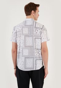 Camisa de manga corta en tejido ligero, con un fondo blanco y patrones y diseños intrincados en negro, acentos cuadrados y un corte relajado.