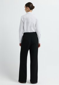 Witte blouse met lange mouwen en een kraag, gecombineerd met zwarte high-waisted broek. Gladde stof met een getailleerde pasvorm en knoopaccenten.