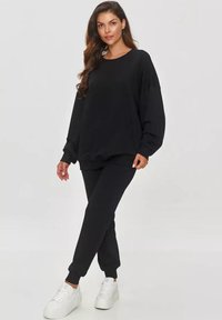 Czarny zestaw bluzy i spodni dresowych wykonany z miękkiego materiału. Posiada długie rękawy, ściągacze przy kostkach oraz luźny krój. W połączeniu z białymi trampkami.