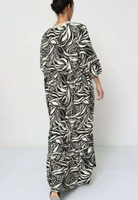 Robe maxi longue en noir et blanc avec un motif de feuilles, coupe décontractée, manches ballons et design à niveaux avec une taille cintrée.