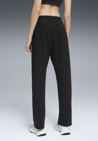 Zwarte sweatpants met een brede tailleband, rechte pijpen en een zachte textuur. Gecombineerd met witte sportschoenen, bekeken van achteren.