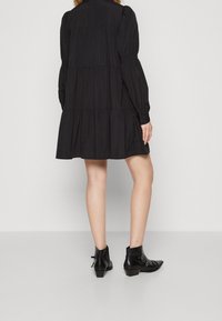 Black tiered dress with long sleeves and gathered cuffs. Features a collar and a swing silhouette, complemented by black ankle boots.