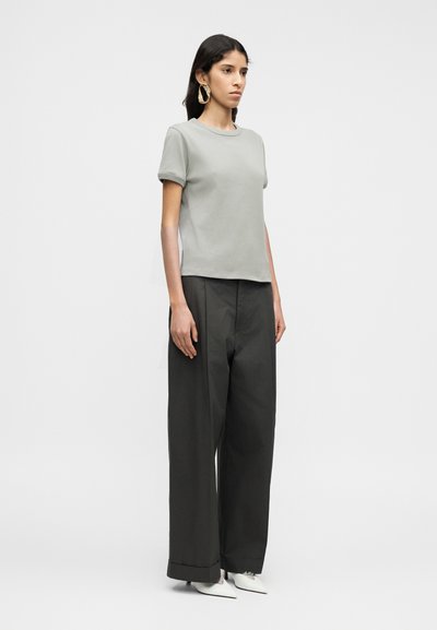 Ανοιχτό γκρι κοντομάνικο μπλουζάκι με στρογγυλή λαιμόκοψη, συνδυασμένο με φαρδιά, σκούρα γκρι ψηλόμεσα παντελόνια και λευκά μυτερά παπούτσια.