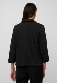 Chaqueta negra con cuello, mangas de tres cuartos y corte recto. Textura suave con sutiles detalles de costura a lo largo de las costuras.