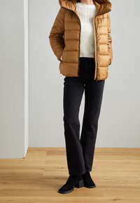 Brun pufferjakke med hætte, strikket cremesweater, sorte højtaljede jeans og sorte ankelstøvler med blokhæl på trægulv.