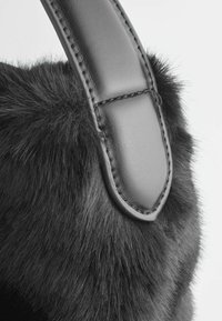Sac en fausse fourrure noir avec une bandoulière en cuir noir lisse. Couture détaillée sur la bandoulière, textures contrastées de fourrure et de cuir.