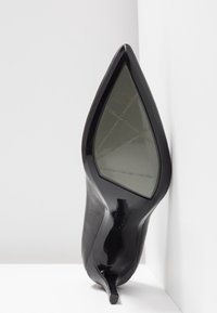 Chaussure noire à talon haut avec un bout pointu et une finition brillante. Présente un talon aigu mince et un logo embossé sur la semelle.