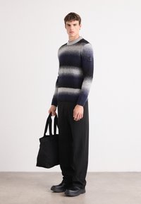 Strickpullover mit navy-, grau- und weißen Streifen, Rundhalsausschnitt, langen Ärmeln, kombiniert mit schwarzen Hosen und einer schwarzen Tragetasche.