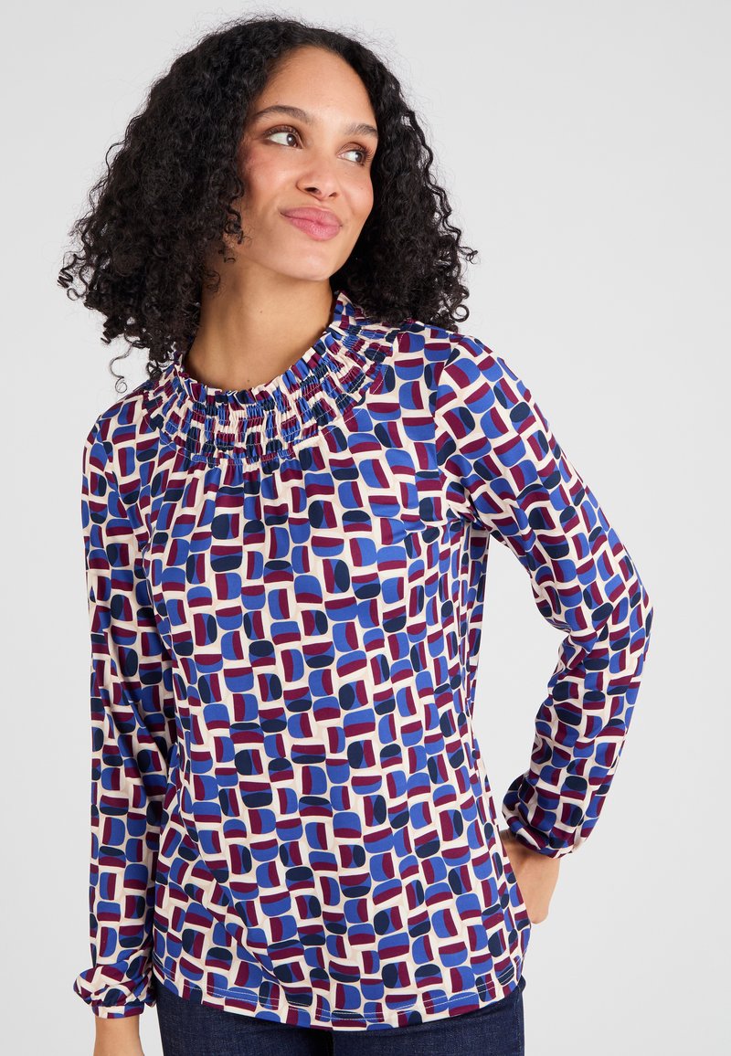 Blusa a maniche lunghe con scollo arricciato, realizzata in tessuto leggero con un motivo geometrico multicolore in blu, rosso e crema.