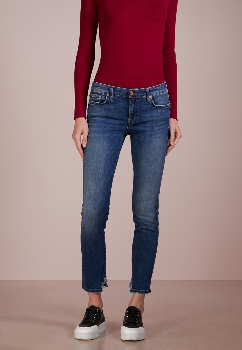 Mörkblå skinny jeans med en urtvättad textur, framfickor och fransad nederkant. Kombineras med svarta plattforms sneakers och en vinröd långärmad topp.