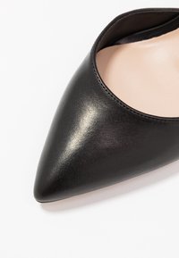 Černá špičatá bota z hladké kůže s nízkým střihem a béžovou vnitřní podšívkou. Žádné viditelné kovové části ani vzory.