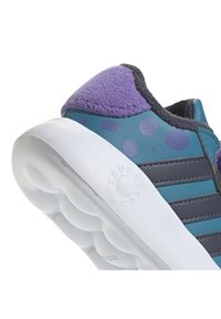 Zapatilla deportiva con un acento púrpura difuso, parte superior color aqua con lunares azules, rayas grises y una suela blanca redondeada.