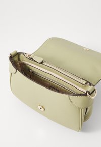 Lys grøn læder crossbody taske med en buet klap, guldt hardware, lynlåslomme og en glat tekstureret overflade.
