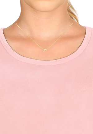 Goldene Halskette mit einem Anhänger in Form des Unendlichkeitssymbols, ausgestattet mit einer dünnen Kette und glatter Textur, getragen über einem hellrosa Oberteil.