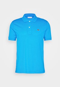 Polo azul hecho de algodón; presenta un cuello clásico, tapeta de dos botones y un pequeño logo de Lacoste bordado en el pecho.