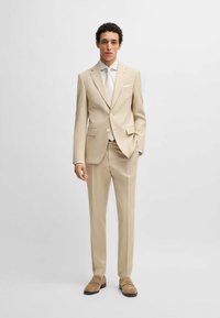 Completo beige chiaro caratterizzato da un giaccone a un bottone con due bottoni, revers a dente di cane e pantaloni con linea piatta. Completato con una camicia bianca e una cravatta.
