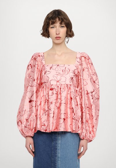 Blusa floral con mangas abullonadas, escote cuadrado, en rosa con patrones de flores rojas. La tela parece texturizada, combinada con una falda de mezclilla azul.