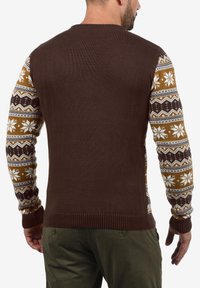 Brun tröja med mönstrade ärmar i nyanser av kräm och brunt, med geometriska och snöflinge mönster. Ribbade muddar och nederdel.