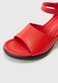 Red leather sandal with a wide strap, open toe design, and a black rubber sole. Smooth texture and minimal design details.
