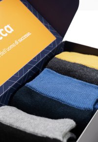 Box mit Socken, die vier Paar in verschiedenen Farben enthalten: Schwarz, Gelb, Blau und Grau. Gestrickte Textur, jedes Paar mit unterschiedlichen Farbbanden.