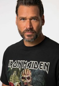 Černé bavlněné tričko s potiskem grafiky "Iron Maiden" a detailním ilustračním zobrazením zombie obličeje. Kulatý výstřih a krátké rukávy.