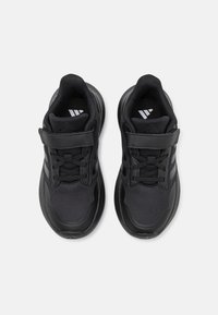 Scarpe da ginnastica nere con tomaia in rete e pelle sintetica, dotate di una fascetta in velcro e lacci, superfici testurizzate e dettagli di branding sottili.