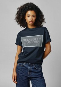 Navyblauwe katoenen T-shirt met een rechthoekige witte graphic met de tekst "RED BULL RACING", gecombineerd met blauwe denim jeans.