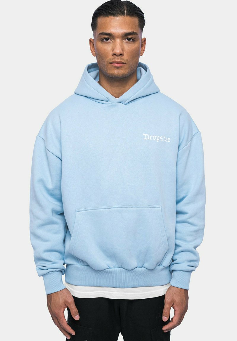 Helleblaue Kapuzenjacke aus weichem Material, mit einer Vordertasche, gerippten Bündchen und einem kleinen weißen Logo auf der Brust.