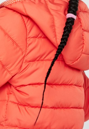 Enfant portant une doudoune orange vif avec une capuche, montrant une longue queue de cheval tressée noire attachée avec un élastique rose.