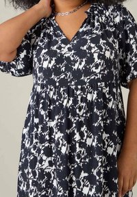 Blommönstrad klänning i svart och vitt, med V-ringning, korta ärmar och en avslappnad passform med en rynkad kropp.