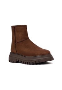 Bruine suède enkellaars met een stevige rubberen zool, ronde neus en minimale stikseldetails, wat zorgt voor een strakke en moderne uitstraling.