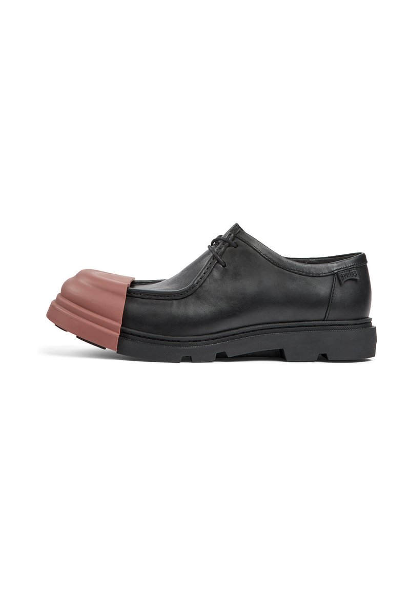 Zapato de piel negro con una puntera de goma marrón redondeada, diseño de perfil bajo y cierre con cordones, que cuenta con una suela texturizada y un minimalismo en la marca.