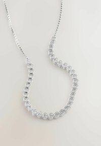 Ezüst nyaklánc, amelyen egy ívelt vonalba rendezett tiszta, kerek drágakövek vannak fém láncszemekbe foglalva, egyszerű világos háttéren.